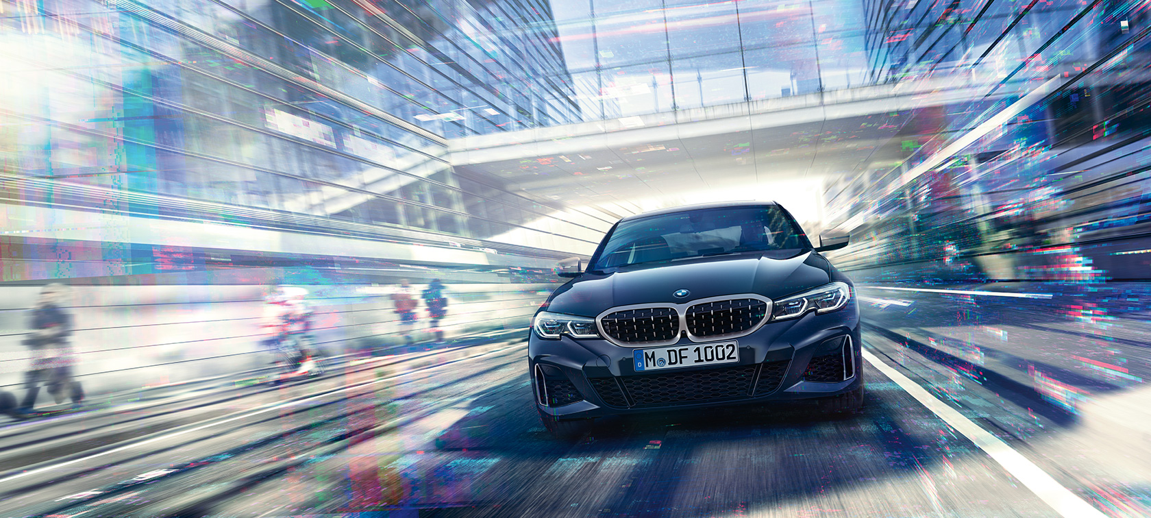 BMW Serie 3 Sedán, vista frontal del BMW M340i xDrive. Vista frontal del BMW M340i xDrive Sedán en movimiento entre edificios de cristal urbanos.