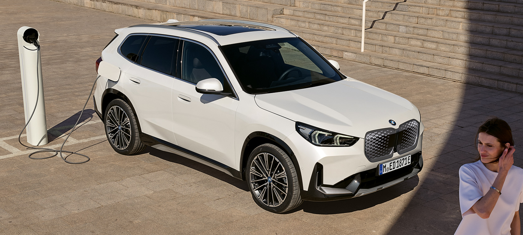 BMW iX1 U11 BEV, vista lateral cargando BMW iX1 U11 BEV 2022 Mineral White metalizado, vista lateral de dos tercios cargando, escalera