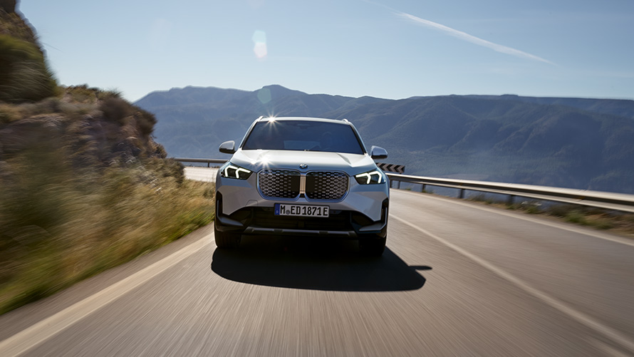 BMW iX1 U11 BEV 2022 Vista frontal BMW iX1 U11 BEV 2022 Mineral White metalizado, vista frontal, en marcha por una carretera de montaña