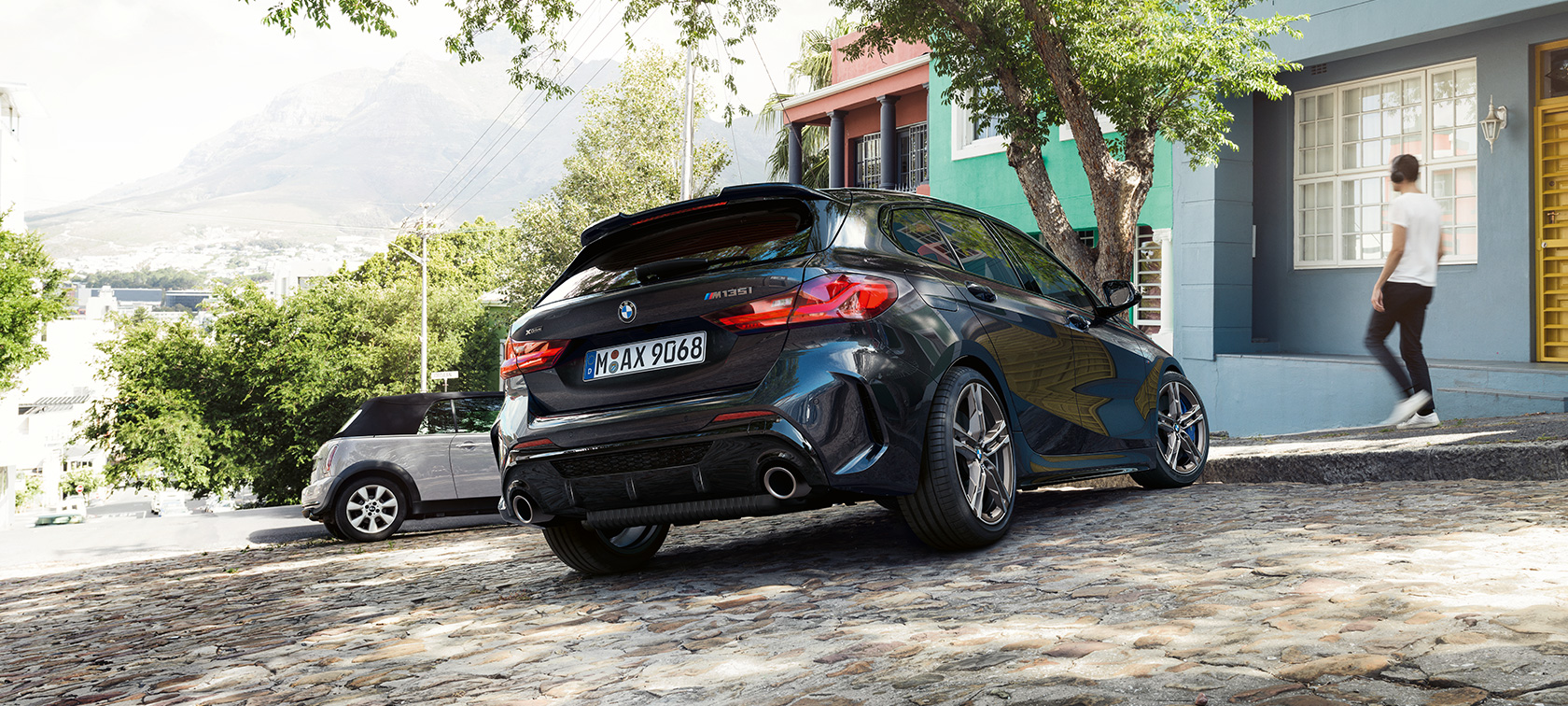BMW M135i xDrive, vista trasera de tres cuartos. BMW M135i xDrive en Black Sapphire metallic, vista trasera de tres cuartos, estacionado frente a un edificio residencial.