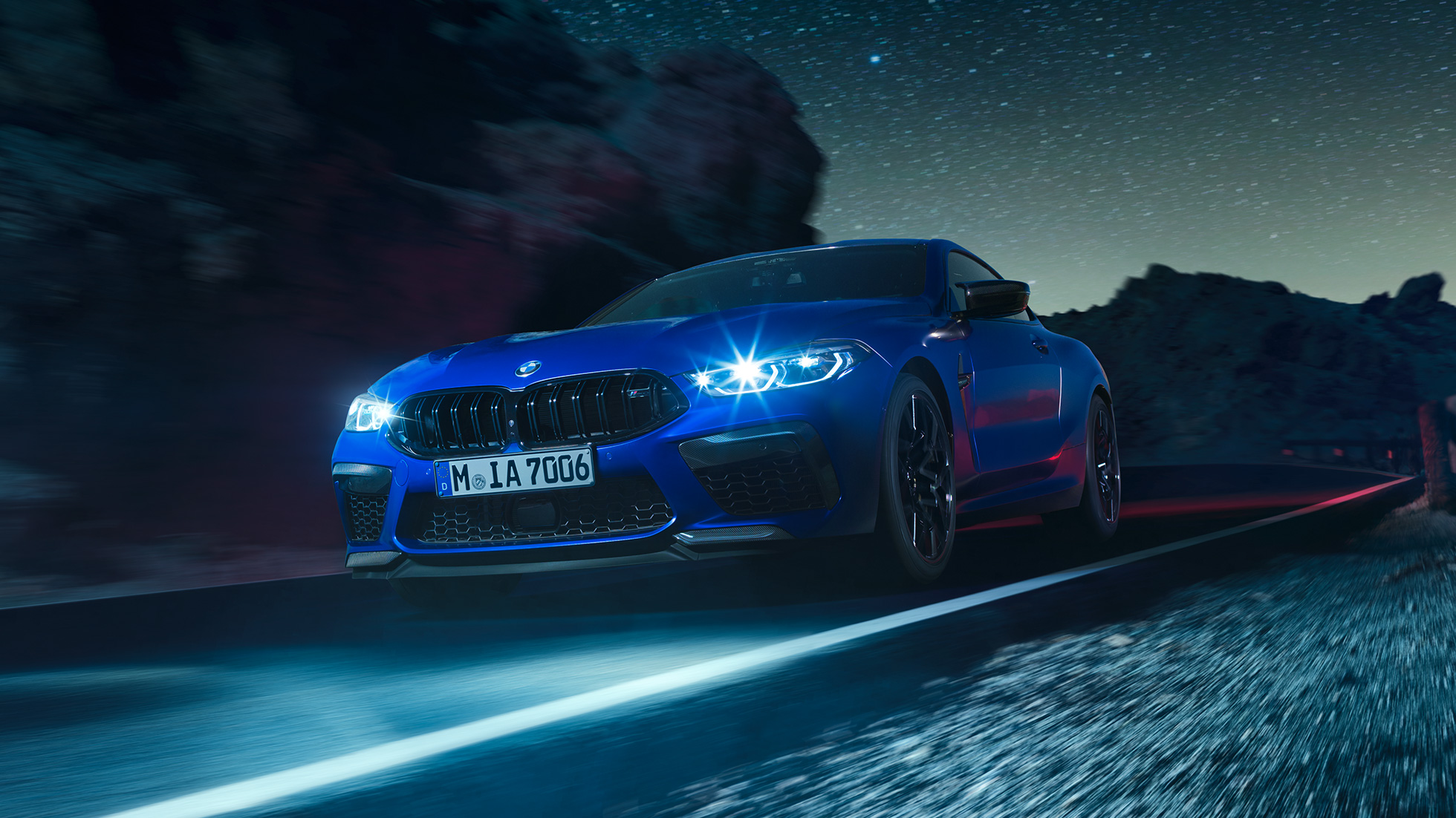 Conduciendo el BMW M8 Competition Coupé, vista frontal tres cuartos. BMW M8 Competition Coupé en Marina Bay Blue metálico con luces LED iluminadas, vista frontal tres cuartos, conduciendo de noche.