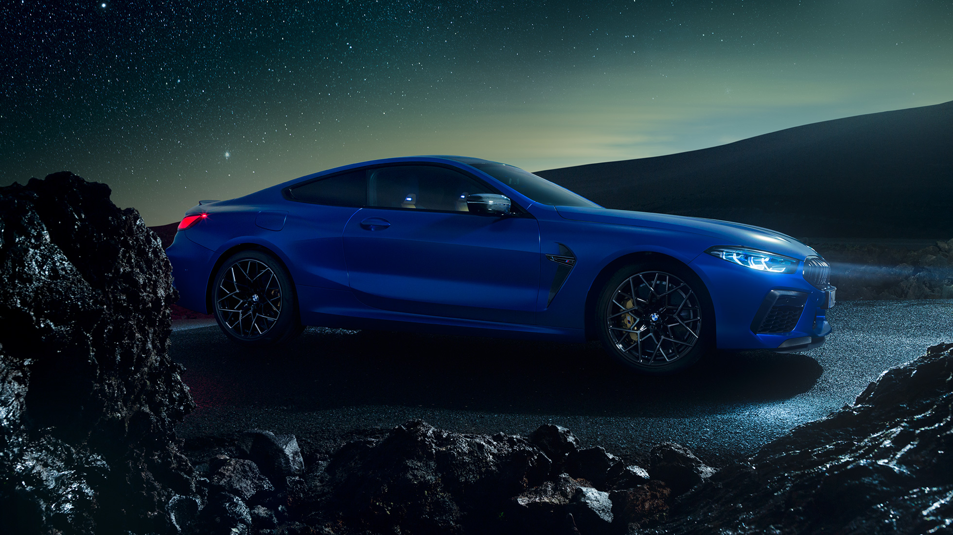 BMW M8 Competition Coupé, vista lateral tres cuartos. BMW M8 Competition Coupé en Marina Bay Blue metálico, vista lateral tres cuartos en alto de noche.