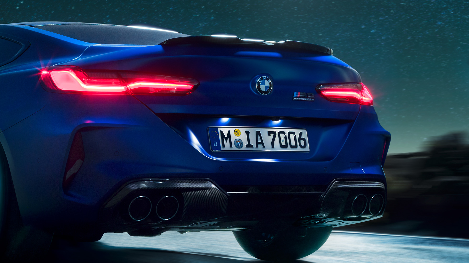 Difusor M en Carbon Black. BMW M8 Competition Coupé en Marina Bay Blue metálico, acercamiento de la parte trasera de noche con diffusor M en Carbon Black.