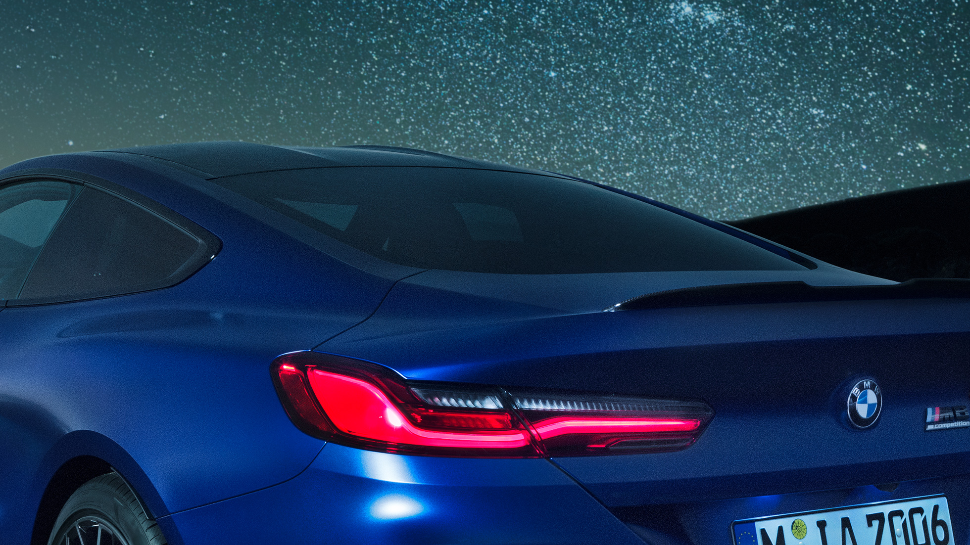 Spoiler trasero M BMW M8 Competition Coupé en Marina Bay Blue metálico, acercamiento nocturno del área del hombro con spoiler trasero M en Carbon.