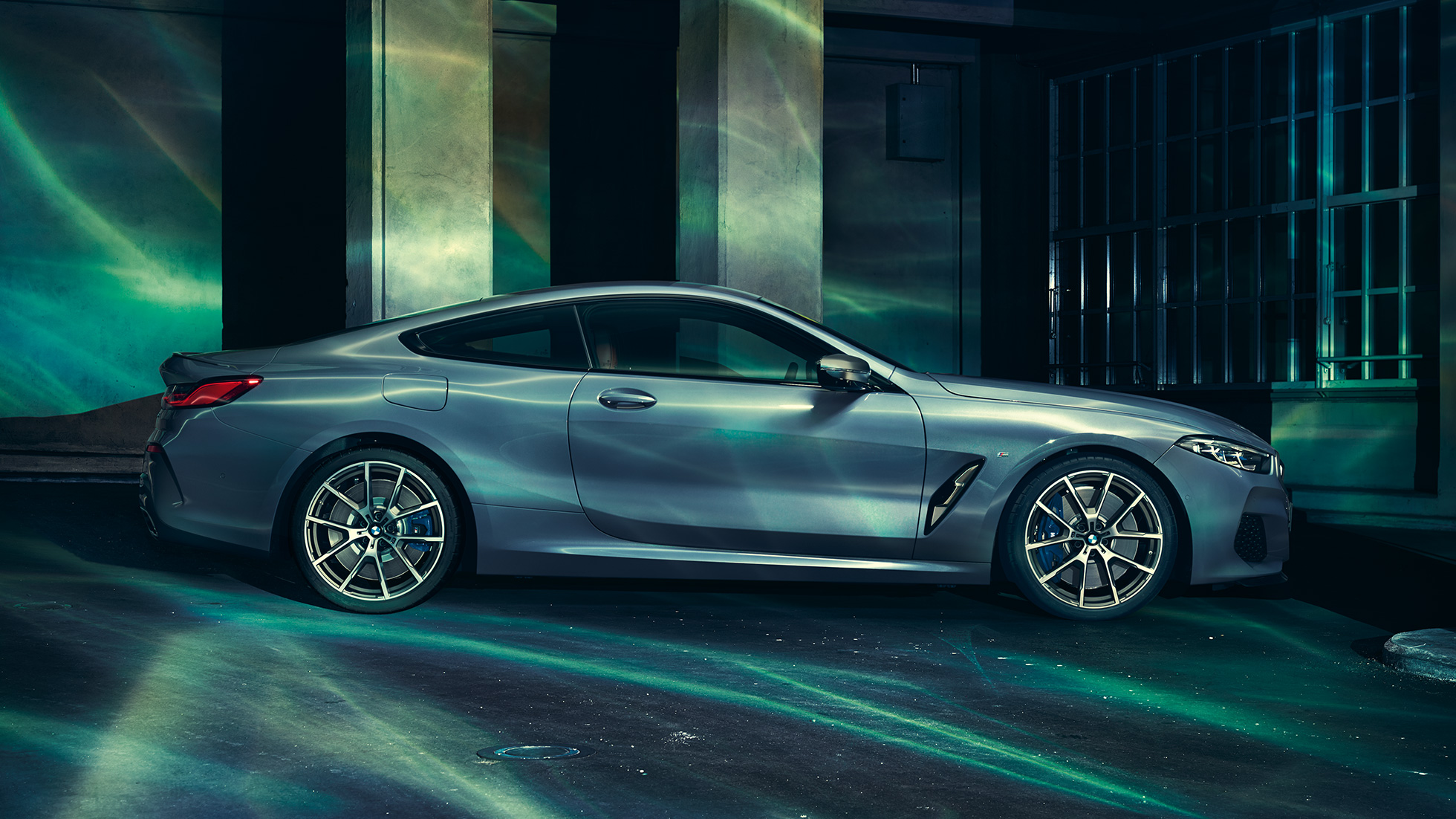 BMW M850i xDrive Coupé, vista lateral. BMW M850i xDrive Coupé en Barcelona Blue metálico, vista lateral, parado frente a un edificio.