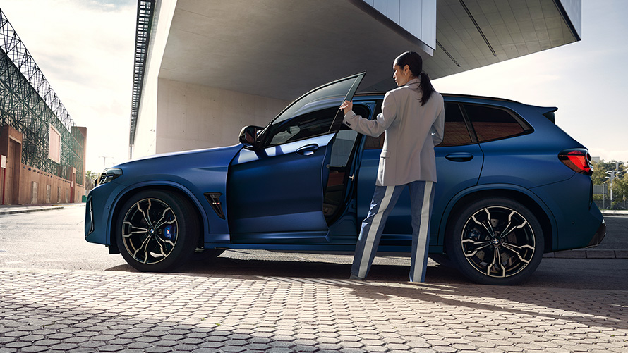 BMW X3 M Competition F97 LCI 2021 Vista lateral con la puerta abierta y modelo femenina BMW X3 M Competition F97 LCI Renovación 2021 Frozen Marina Bay Blau metalizado, vista lateral con la puerta abierta y modelo femenina