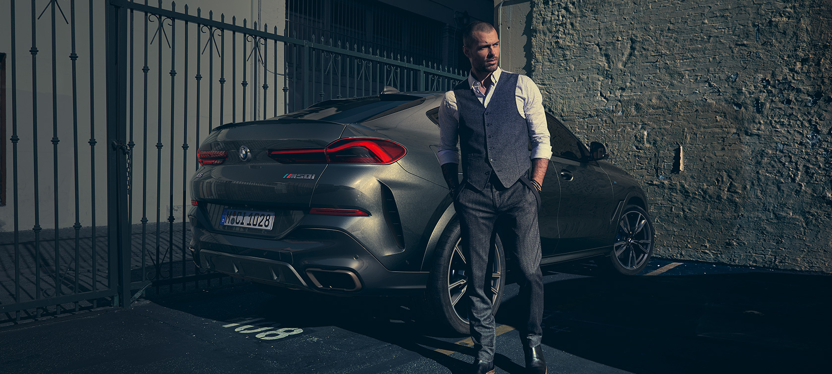 BMW X6 M50i en vista trasera de tres cuartos. Hombre parado junto a un BMW X6 M50i SUV en vista trasera de tres cuartos.